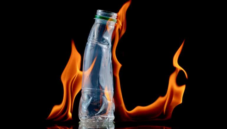 A plastic bottle melts in fire against a black background