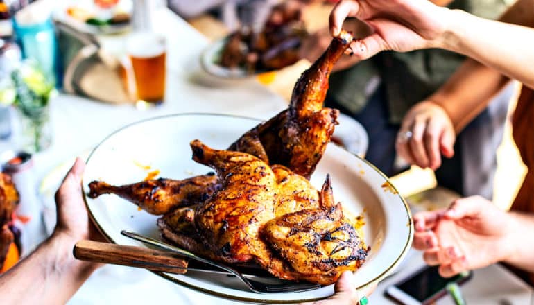 A family serves chicken off a plate as a young child grabs a drumstick