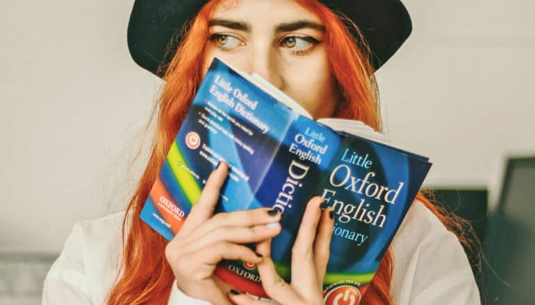 person looks concerned while holding dictionary in front of mouth