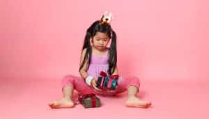 Asian child wearing crown holds wrapped gift on pink background