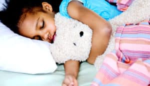 A young girl sleeps while holding a teddy bear.