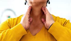 A woman touches either side of her neck where her thyroid glands are.