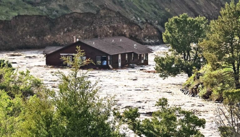 A house floats down the center of a rushing river.