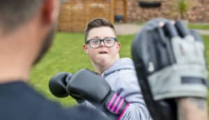 young person with Down syndrome wears boxing gloves and aims to punch target