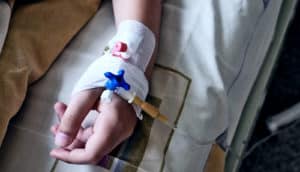 The hand of a child in a hospital bed with an IV line running into it underneath bandages.