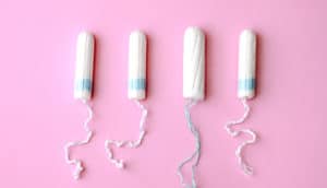 Four tampons lined up on a pink surface.