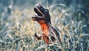 A dinosaur toy standing in some green grass.