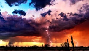 Dark clouds above a desert with lightning cracking and blue skies above.