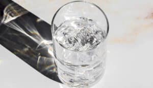 A glass of water on a marble counter with light shining through it.