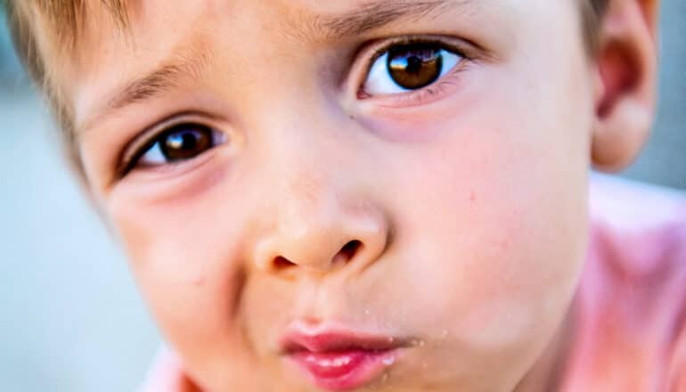 A little boy looks up at the camera with a skeptical expression.