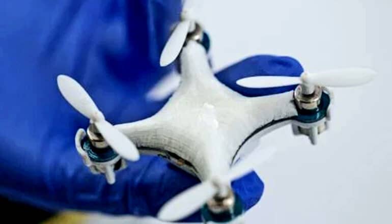 A small drone with four propellers in the hand of a researcher wearing purple gloves.