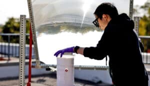 A researcher holds the water splitting device below an angled mirror on the roof of a building.