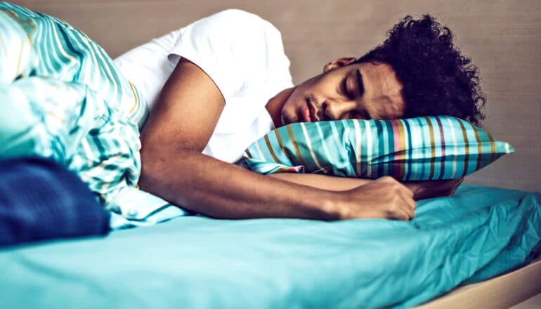 A young man in a white t-shirt sleeps on green sheets.