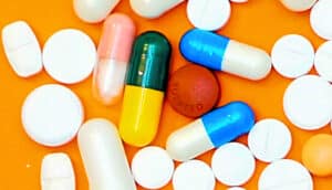 Various white and colorful pills on an orange background.