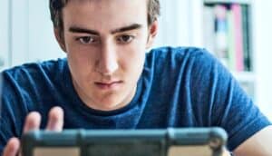 A young man looks down at a tablet while sitting at a table.