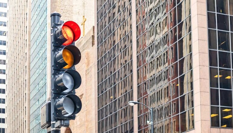 A traffic light with four separate lights with city buildings in the background.