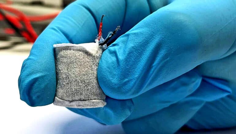 fabric-wrapped, square object held between gloved fingers