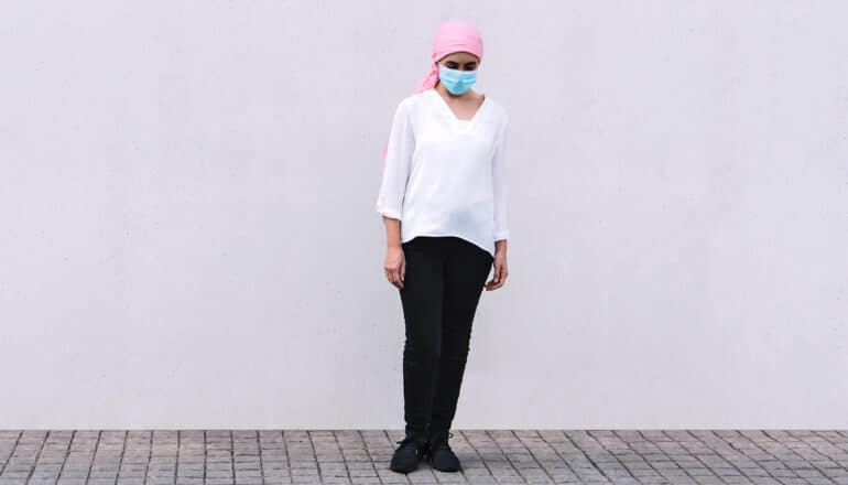 person with pink scarf on head and surgical mask stands alone in blank space