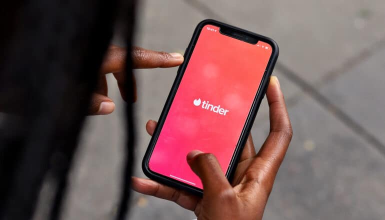 hands of Black person hold phone with Tinder dating app on screen