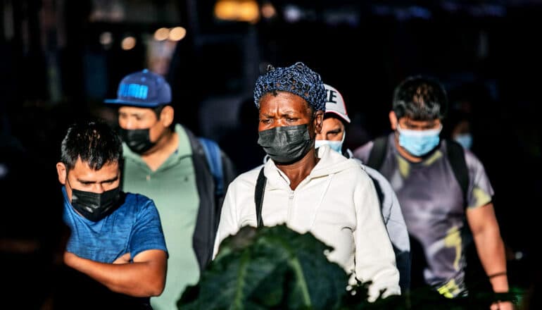 People walk in an outdoor market while wearing face masks for COVID protection.