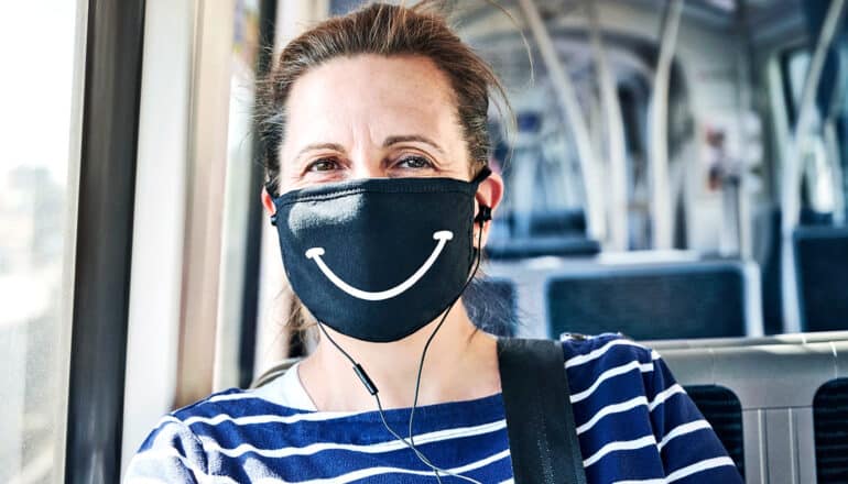 A woman on a bus wears a face mask with a smiley face drawn on it.