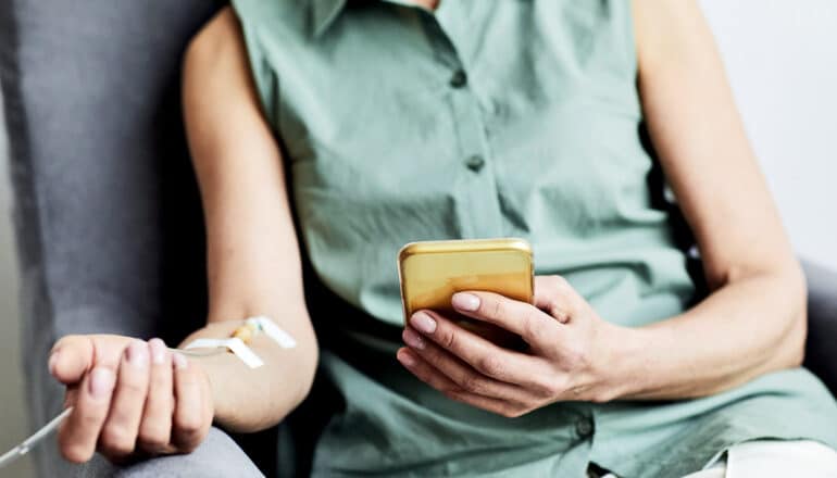 A woman looks at her phone while getting chemotherapy through an IV.