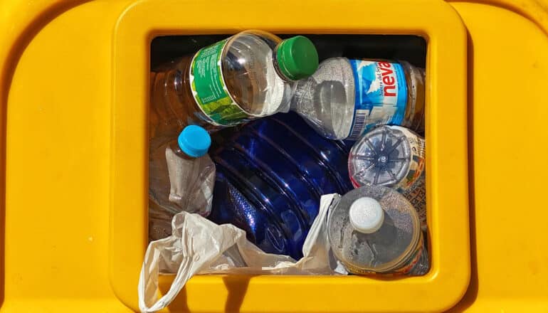 plastic bottles in opening of yellow recycling bin