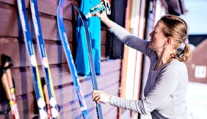 A woman waxes her skis as they lean against a wall.