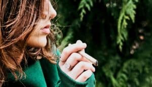 A teenager smokes a joint in the woods.