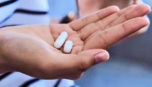 A young person holds two white pills in one hand.