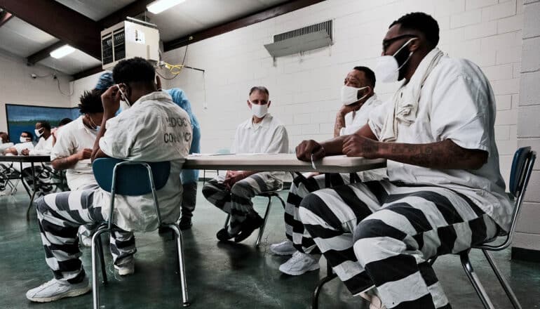 seated people wearing prison uniforms and masks