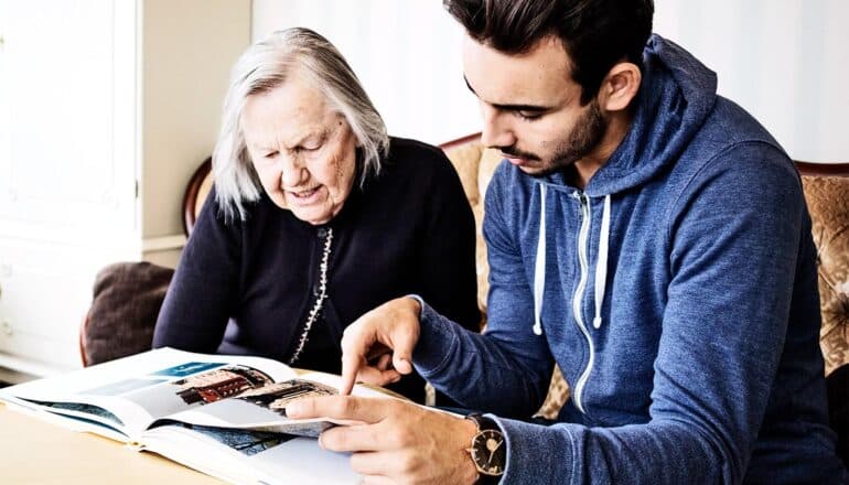 A young man reads a book with an older woman.