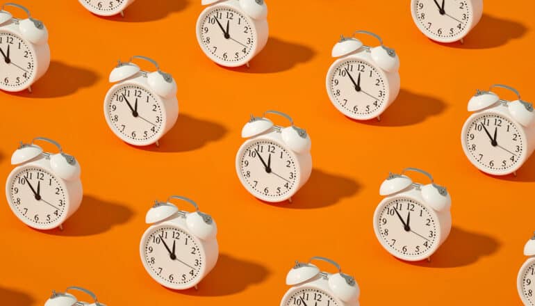 White alarm clocks in rows on an orange background.