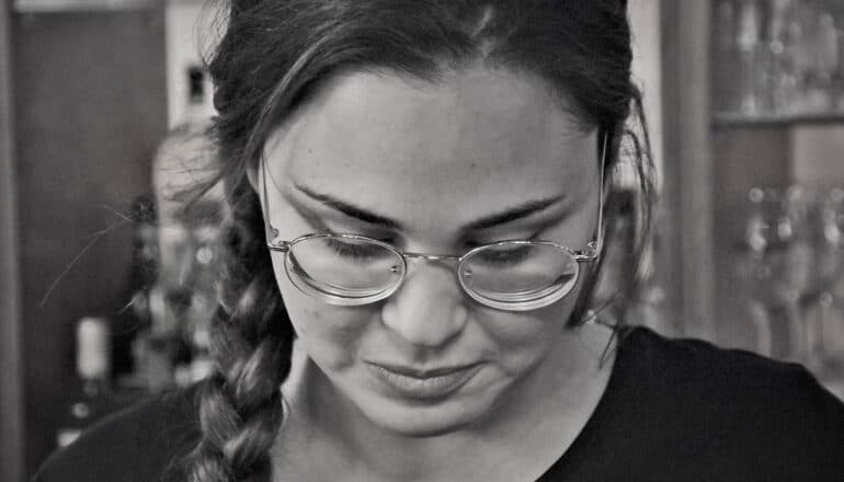 A young woman wearing glasses looks downward with a pained expression.