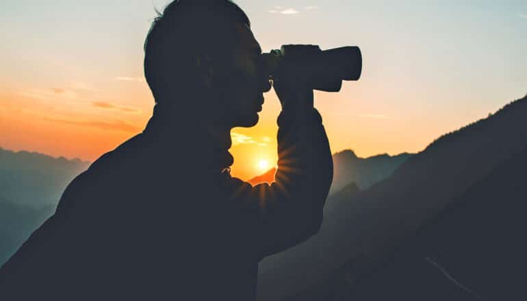 A person looks through binoculars at dawn.