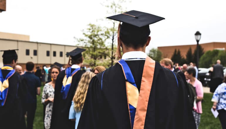 A college graduate in cap and gown in a crowd of graduates and family.