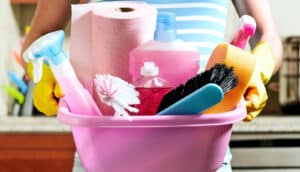 A person holds a pink tub filled with cleaning products.