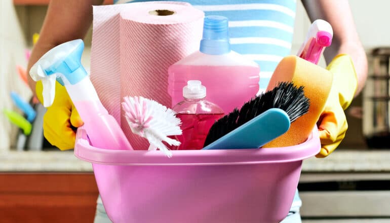 A person holds a pink tub filled with cleaning products.