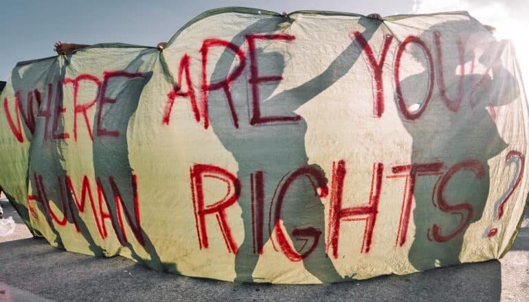 people appear in silhouette behind "where are your human rights?" banner