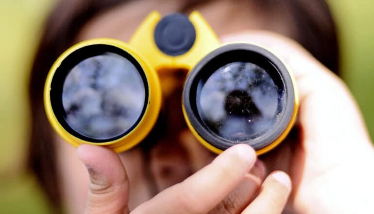 A young child holds up a pair of yellow binoculars to their eyes.