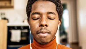 A young man with headphones in his ears closes his eyes for meditation.