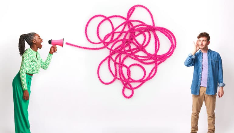 A woman speaks through a megaphone that has string coming out of it and getting tangled while a man holds his hand up to his ear.