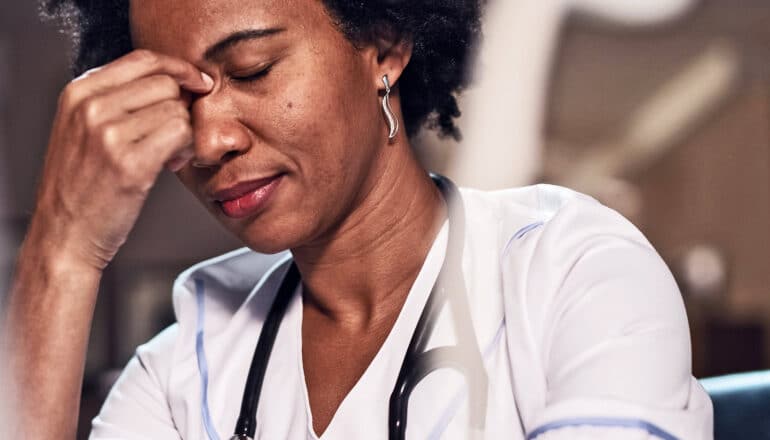 A nurse puts her fingers to the bridge of her nose while sitting at a desk.