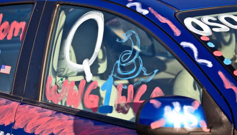 A car has a "Q" painted on the window along with a snake.