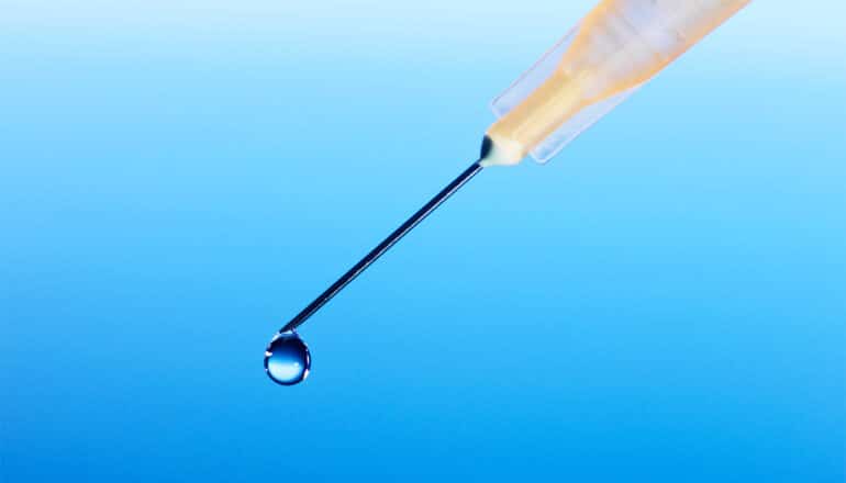 A syringe with a drop of liquid coming out of the needle.