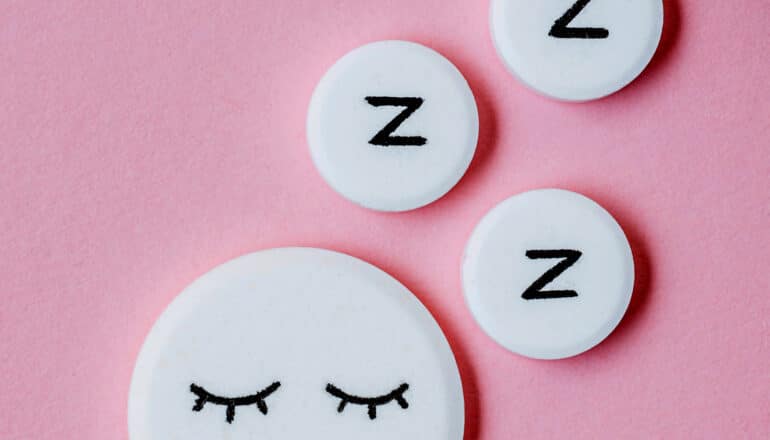 A white pill with closed eyes drawn on it and smaller white pills with the letter z on them indicating sleep.