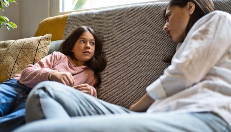 A mother and daughter talk while sitting on a couch.