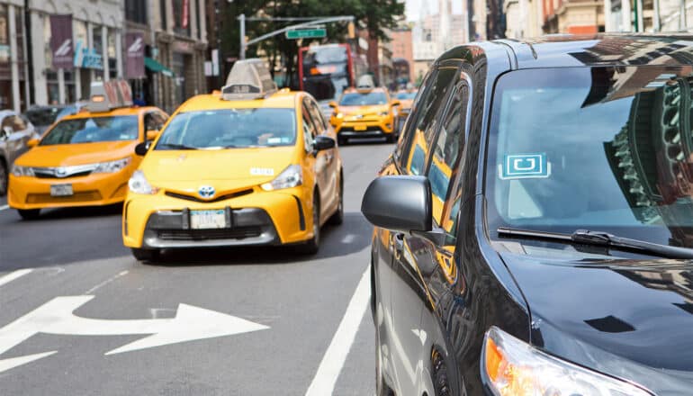 An Uber car in one lane with yellow taxis in other lanes on a city street.