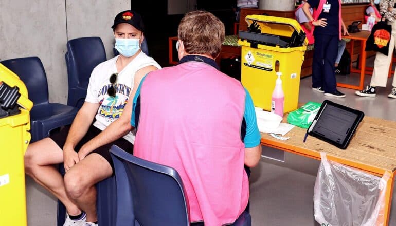 A person gets a Covid vaccination from a health worker wearing a pink vest.