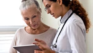 A doctor points to a tablet computer while speaking with a patient.